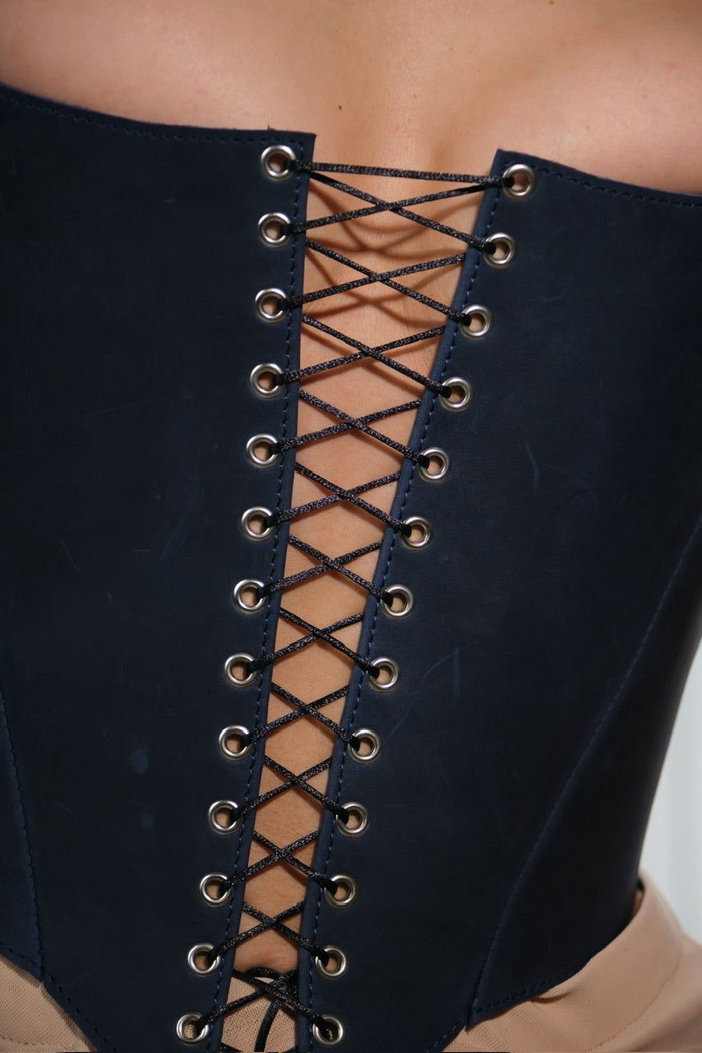 A close-up view of a person wearing a black corset with a lace-up design.