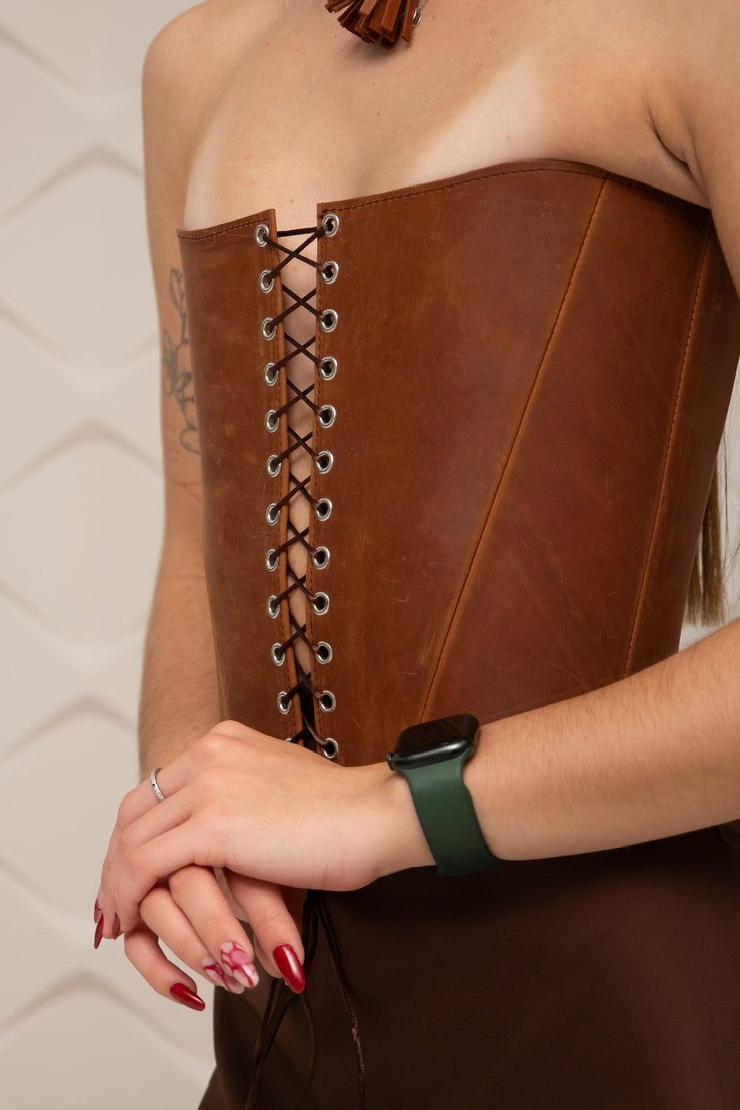 A woman wearing a brown leather corset with a green watch on her wrist.