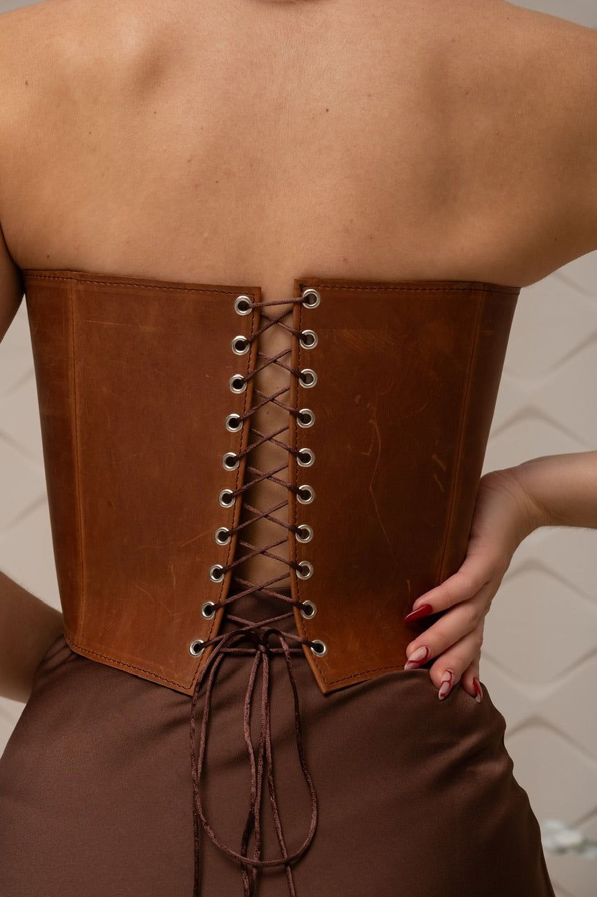 a close-up view of a person's back, wearing a brown leather corset with a lace-up detail.