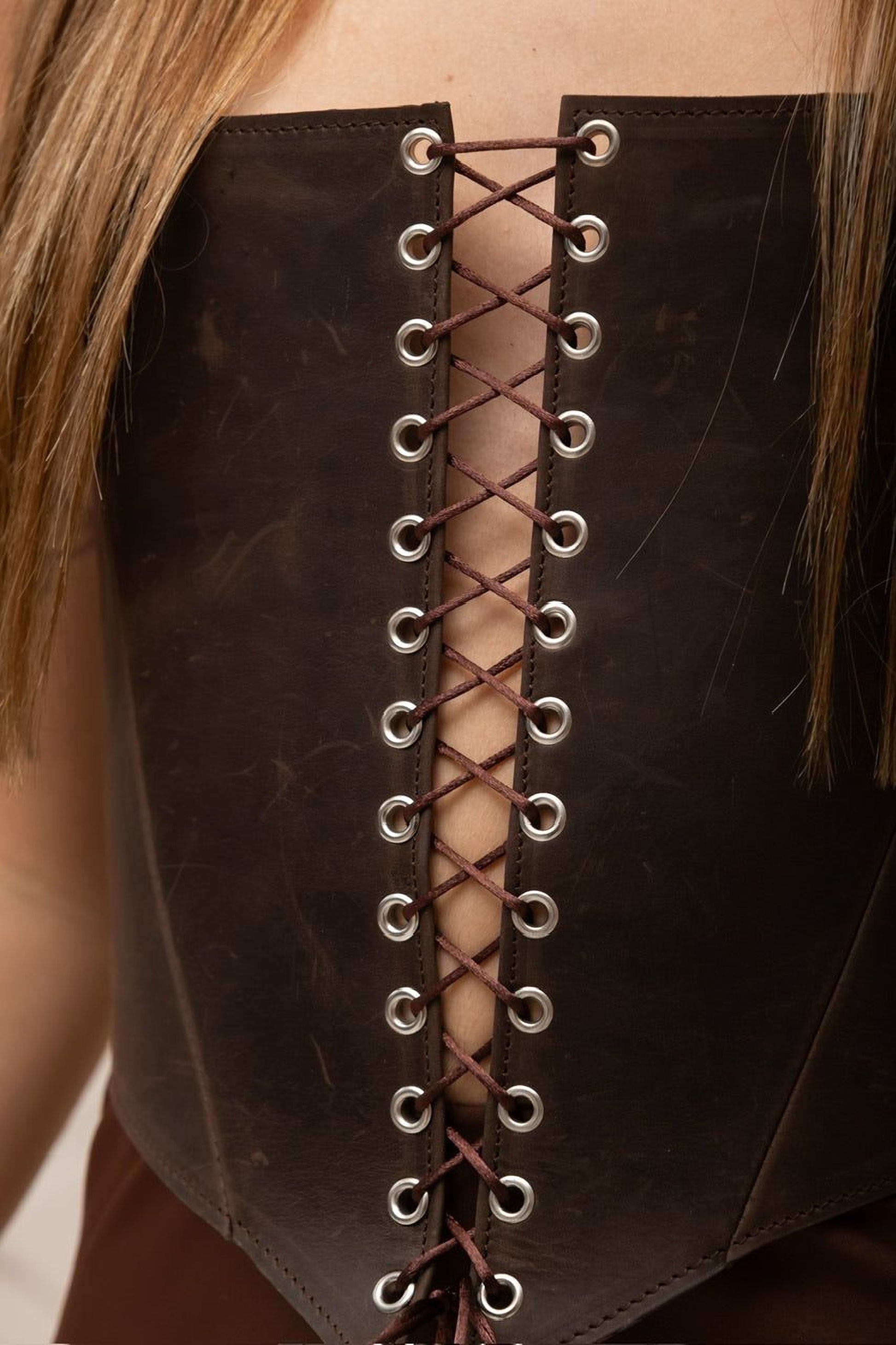 A close-up view of a woman's torso wearing a brown leather corset with a lace-up back.